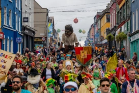 A 5-metre-high giant walking amongst a crowd of people in colourful clothes and costumes