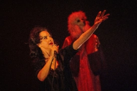 A woman with her arm outstretched, looking up to her left. Behind her is a dog mannequin with fluffy hair and long ears.