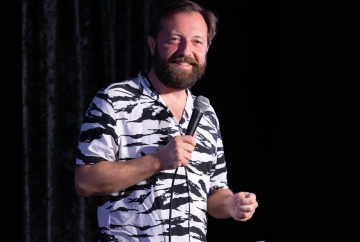 Andrew Maxwell performing standup against a black background. Photo cred: @craicdencomedy