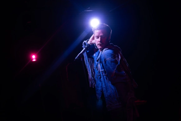 Man dancing with his eyes closed wearing a blue denim jacket with a spotlight behind him