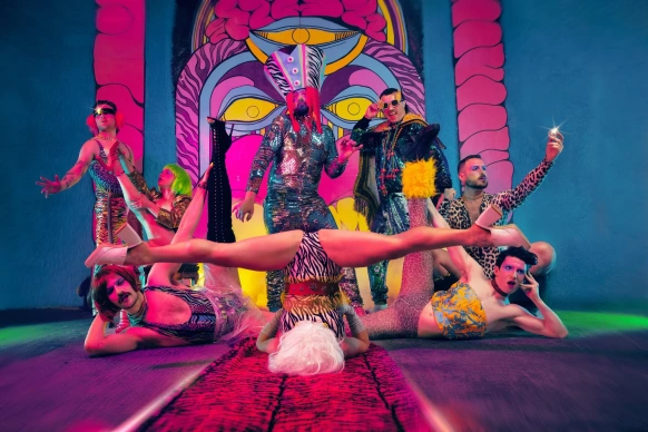 Multicoloured image with vibrant shades of blue, purple and pink. Seven dancers pose in different positions